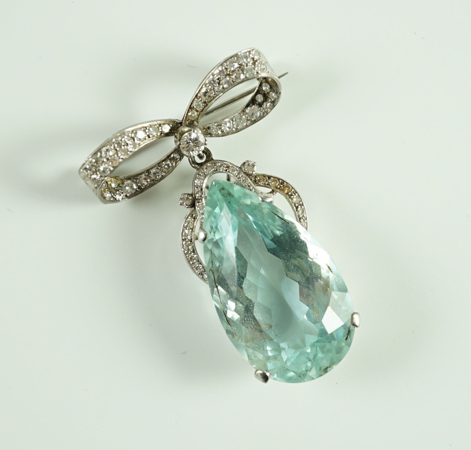 A mid 20th century continental white gold, facet cut pear shaped aquamarine and diamond set drop pendant, on a diamond set ribbon bow brooch